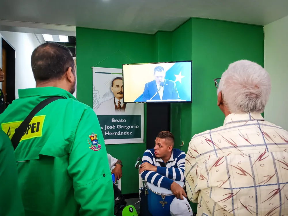 Militantes del partido Copei, escuchan en un televisor al candidato presidencial Juan Carlos Alvarado.